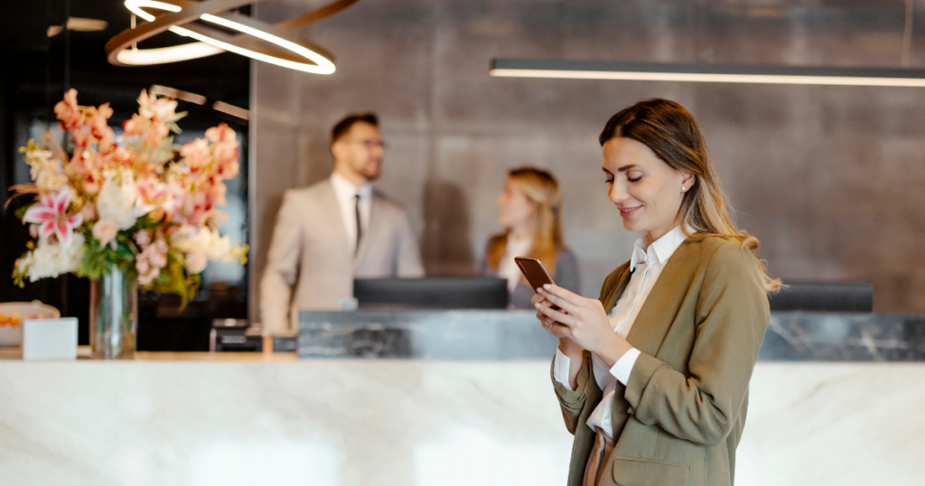 Woman at a hotel lobby, smiling and checking her mobile phone for any special hotel deals & offers