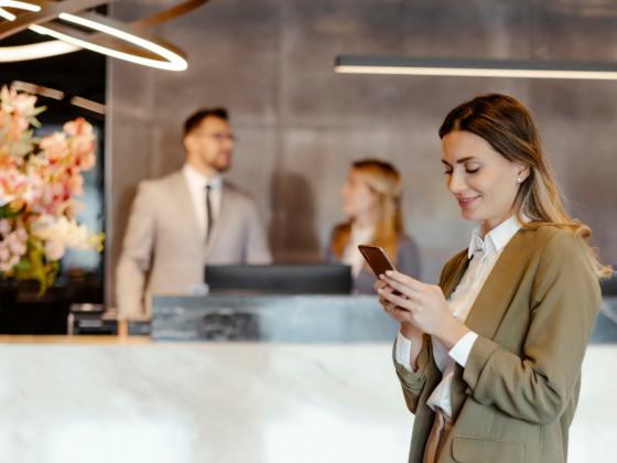 Woman at a hotel lobby, smiling and checking her mobile phone for any special hotel deals & offers