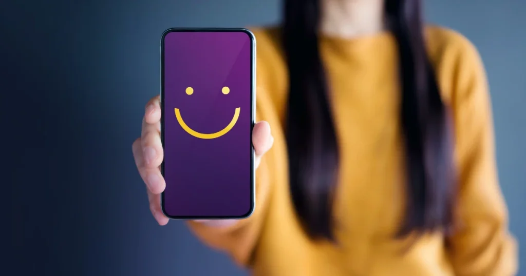 A woman hand holding a mobile phone with a smiley face on screen.