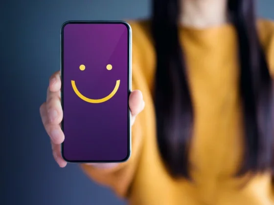 A woman hand holding a mobile phone with a smiley face on screen.